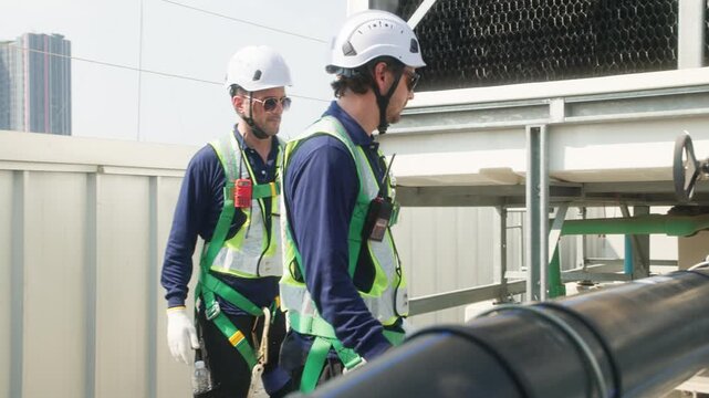 Two industrial technicians in safety helmets and vests adjusting a large valve on a heavy pipeline system at an industrial facility.