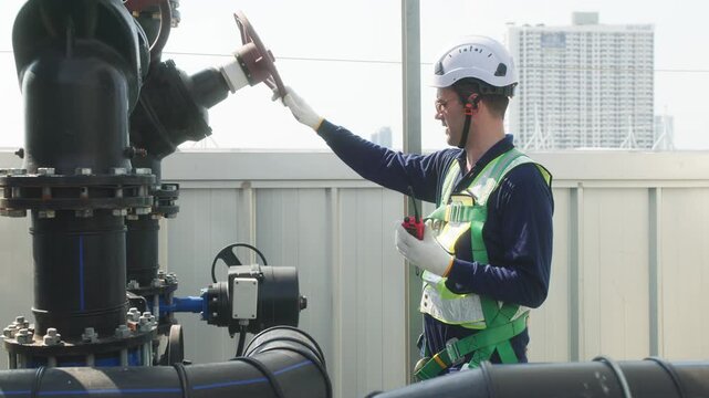 Two industrial technicians in safety helmets and vests adjusting a large valve on a heavy pipeline system at an industrial facility.
