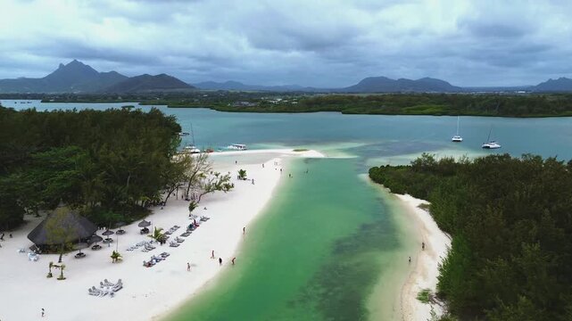Aerial view capturing the iconic coastal layout of Ile aux Cerfs (Deer Island), Mauritius. Winding turquoise lagoon channel with clear shallow water, bordered by an expansive white sand beach featurin