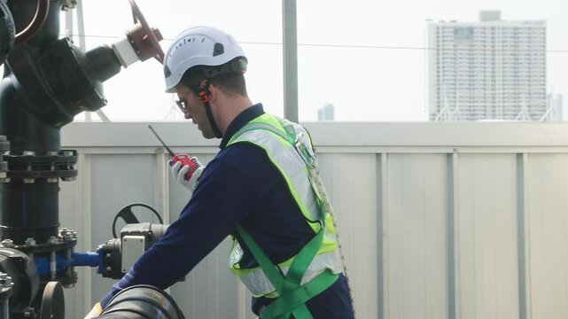 Two industrial technicians in safety helmets and vests adjusting a large valve on a heavy pipeline system at an industrial facility.