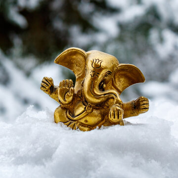 Golden Ganesha statue on fresh winter snow with blurred forest background celebrating peace and spirituality
