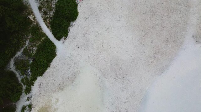 Aerial drone shot capturing a bird's-eye perspective of a rugged coastline in Mauritius. The right side features a patch of pristine white sand beach covered in fractured, dark black volcanic lava roc