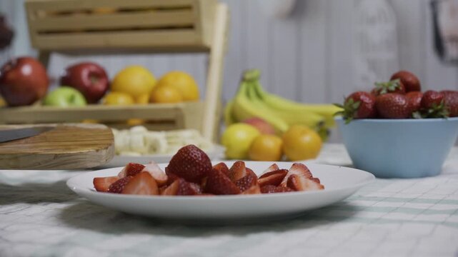 Chef scrapping cut up strawberries onto plate near other fruit - closeup shot