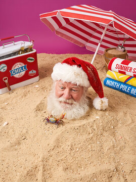 Funny Santa Claus buried in beach sand during summer vacation looking at a small crab
