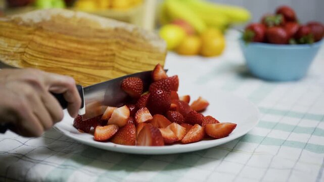 Closeup of knife being used to scrape sliced strawberries onto plate