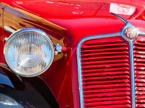 Detail of the front grille, brand logo, and chrome headlight of a classic red vintage Tatra 57 veteran car, known as Hadimrska, at a historic automobile exhibition.