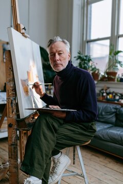 Elderly male painter portrait in a sunlit studio background for artist profile banner and creative workspace design