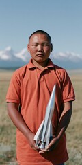 Fototapeta premium Boy holding a silver model rocket in an open field portrait with mountain backdrop for science club poster and educational banner