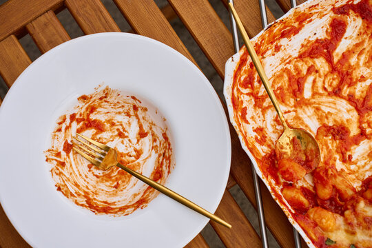 Empty plate with tomato sauce traces beside baking dish with leftover gnocchi