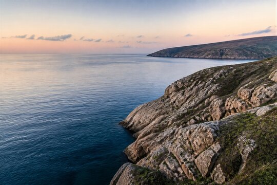 Coastal cliffs meeting calm sea at dusk on rocky shoreline