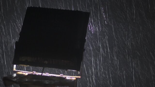 intense rainfall captured at night with raindrops brightly illuminated by a backlit floodlight, creating dramatic streaks against a dark sky with strong atmospheric mood and copy space