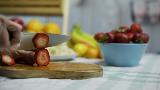 Closeup of person using sharp knife to slice up strawberry on cutting board