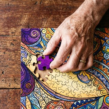 Elderly person places a purple piece into a colorful jigsaw puzzle on a wooden table World Alzheimer Day
