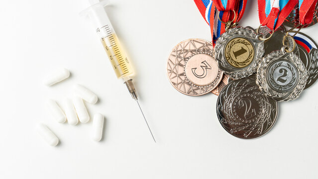 Syringe with yellow liquid sits beside white pills. Multiple medals with ribbons show competition achievements. The scene connects drugs to athletic success