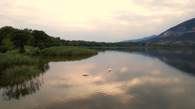 Calm mountain lake drone footage reflecting Alpine peaks and lakeside village at dawn, Brianza Italy