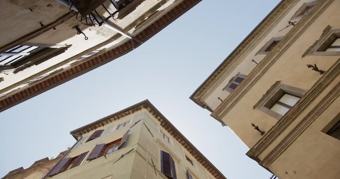 Low angle view of historic Tuscan buildings and shuttered windows framing a clear blue summer sky in Italy