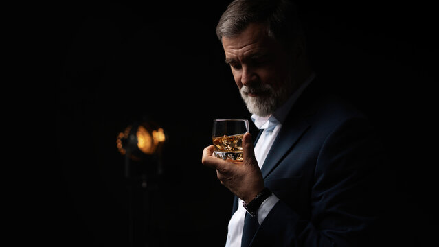 Handsome businessman in stylish suit holding glass whiskey on dark