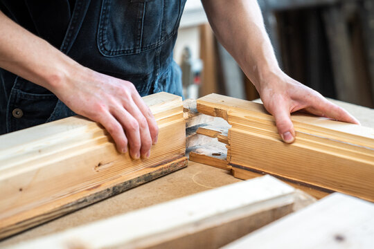 Craftsman assembling restored and refurbished parts of old wooden window frame on workbench, professional woodworker accurately joining two wooden boards with patches at corners for perfect fitting.