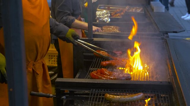 Street food vendor grilling sausages over open flames. Professional cook grilling delicious pork sausages on a large charcoal barbecue with open flames and smoke