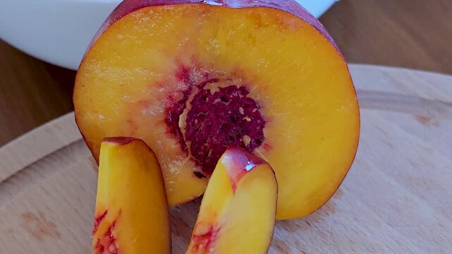 Fresh nectarine sliced into wedges on wooden cutting board by chef in black gloves for elegant serving, close up