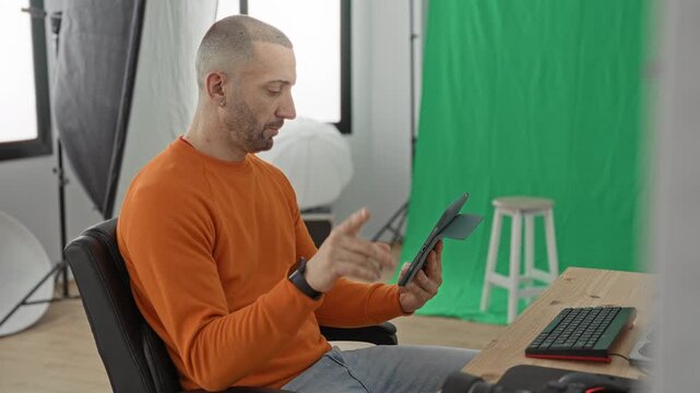 Man holding tablet points finger to screen in studio with green backdrop, softbox and wooden stool; concentration creativity.