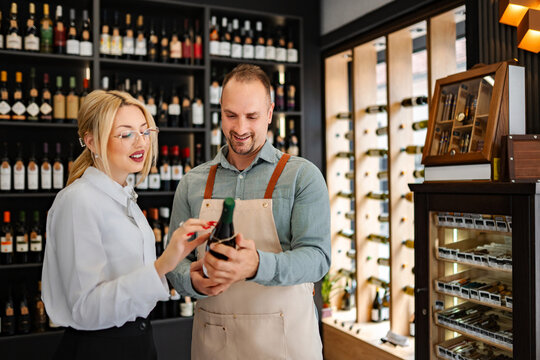Sommelier assisting woman customer choosing wine in shop