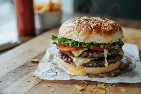A double cheeseburger with melted cheese, lettuce, tomato, and pickles on a sesame seed bun served on parchment paper on a rustic wooden table