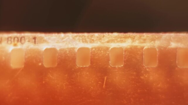Slow motion close up texture and damaged view of warm 35mm film reel with no shots, broken scratched elements, and badly exposed dirty strip from cinematography photographic spool tool in slow mo 4k