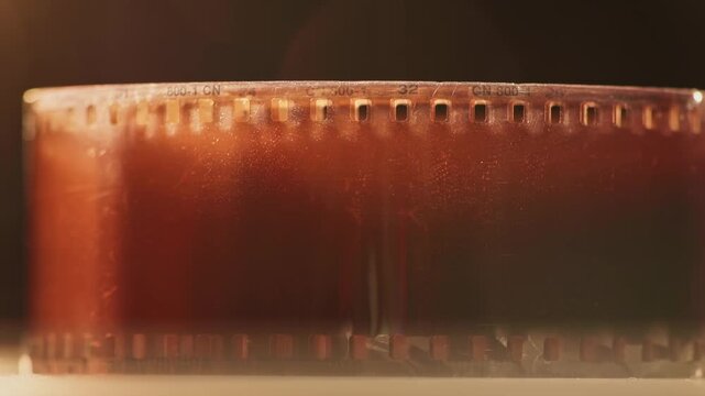 Slow motion close up texture and damaged view of warm 35mm film reel with no shots, broken scratched elements, and badly exposed dirty strip from cinematography photographic spool tool in slow mo 4k