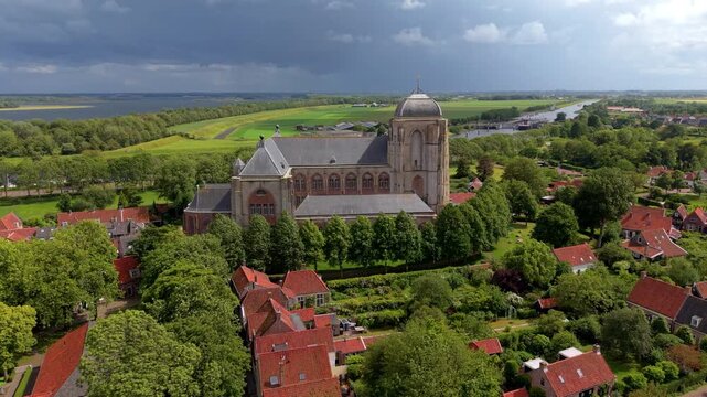 Beautiful high altitude aerial panoramic perspective of historic medieval Grote Kerk church cathedral village red roof houses canal dramatic stormy sky and countryside in sunlight