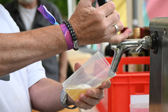 Beer is poured from a tap into a reusable plastic cup at a casual outdoor festival event, concept for sustainable open-air entertainment, fun and cold drinks, selected focus