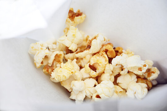Fresh popcorn in a white paper bag, popular sweet snack food at events and in movie theaters, copy space, selected focus