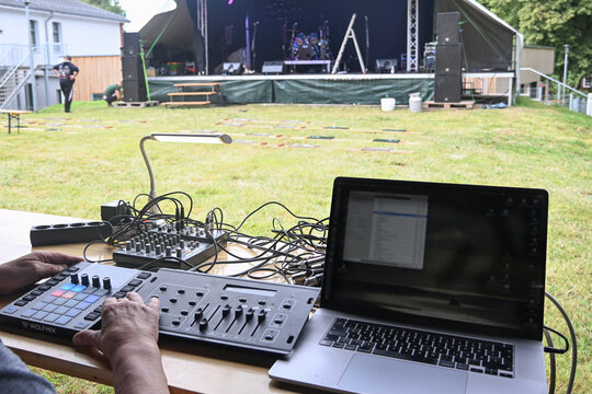 Sound and lighting control equipment on a table far in front of the open-air stage is being tested before an outdoor concert, event technology for a summer festival