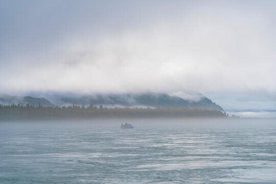 Raft flowing downriver through thick morning mist along Alsek River, Alaska