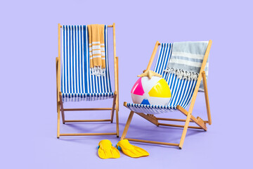 Two striped beach chairs with towels, a colorful beach ball, and yellow flippers on a purple background © Pixel-Shot