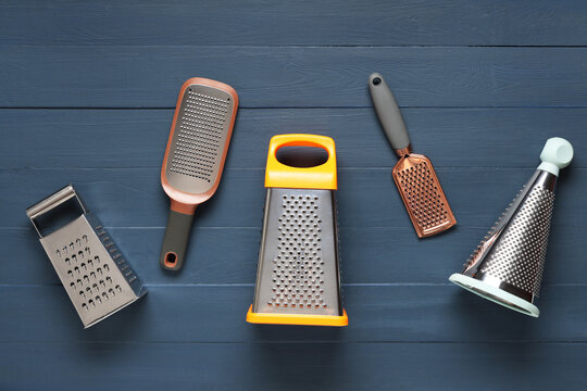 Assortment of kitchen graters and zesters for food preparation on a dark blue wooden background, top view