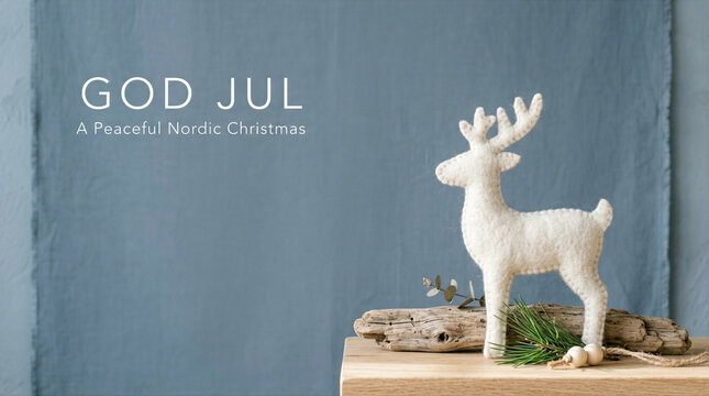 Minimalist Nordic Christmas greeting featuring a white felt reindeer on rustic driftwood with God Jul text against a blue linen background