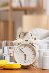Naklejka premium Alarm clock with glass of water and pills on table in room
