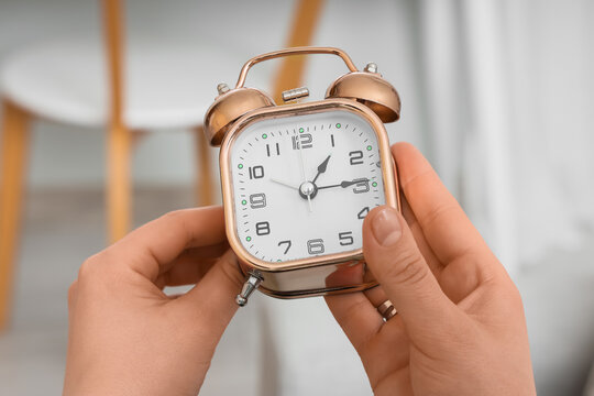 Female hands setting time on alarm clock at home, closeup. Daylight saving time concept