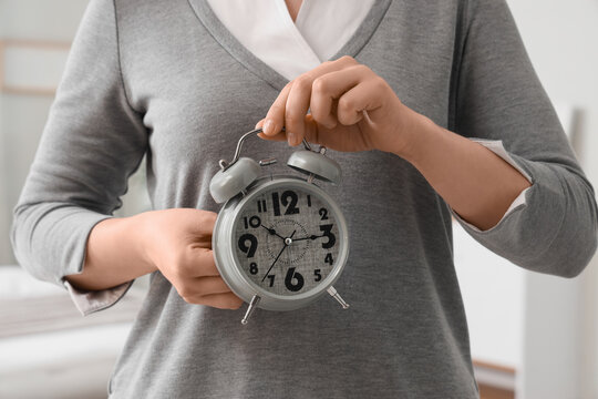 Woman setting time on alarm clock in bedroom, closeup. Daylight saving time concept