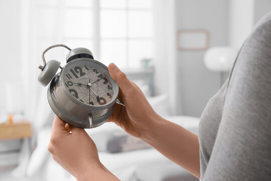 Woman setting time on alarm clock in bedroom, closeup. Daylight saving time concept