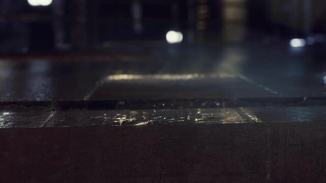 A worker is unpacking a cardboard box in a warehouse. Water droplets are visible on the surface, suggesting recent wet conditions. The lighting is bright and the space is busy.