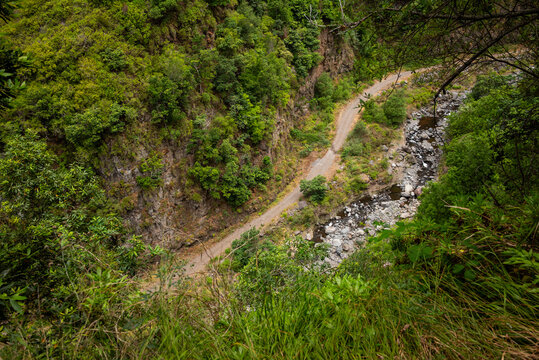 Looking down from the levada trail onto a gravel road and boulder riverbed deep in a subtropical ravine, Levada do Moinho, Ponta do Sol, Madeira, Portugal