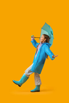 Cute teenage girl in raincoat with blue umbrella on yellow background