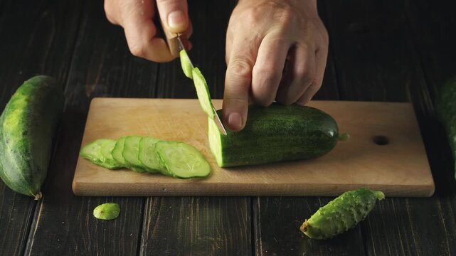 Hands slicing fresh cucumber into thin rounds on a wooden cutting board, with additional cucumbers and slices visible, creating a vibrant kitchen scene focused on food preparation