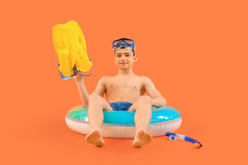 Cute little happy boy with inflatable ring, flippers and snorkeling mask on orange background © Pixel-Shot