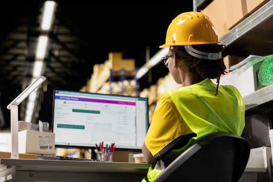 An African American woman uses tracking software in a logistics hub, updating delivery routes and shipment details in real time on a PC.