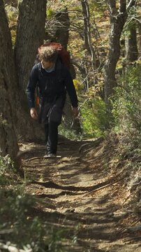 Hiker with a backpack walking along a dirt trail in a dense forest with trees and plants, outdoor adventure, perspective view.