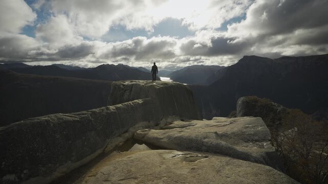 Hiker standing on the edge of a high mountain peak at La Mirada del Doctor, looking out at a reflective lake nestled in Nahuel Huapi National Park, Argentina.