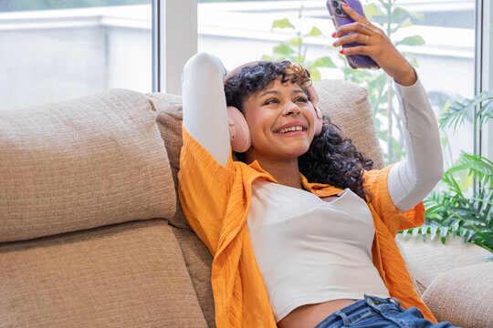 Young woman in casual urban style with headphones and mobile phone at home, excited with joy and happiness